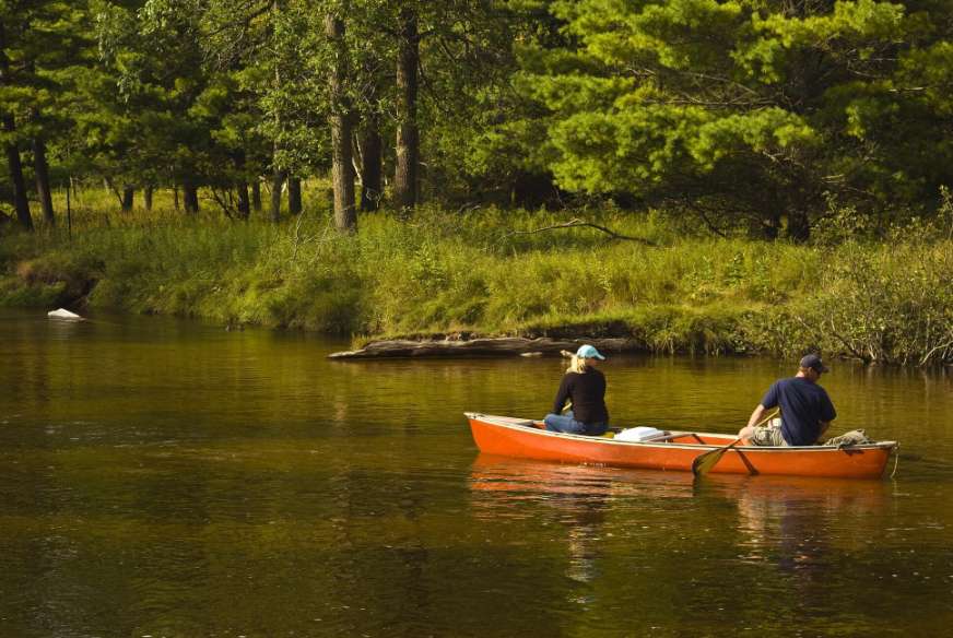 man and woman paddling an orange canoe on river