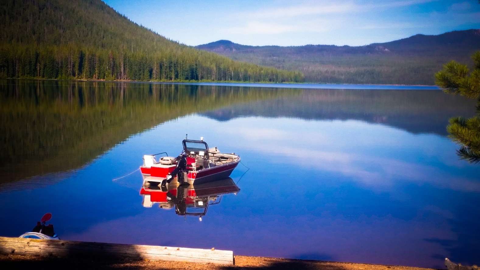 red and white boat in still lake surrounded by forested mountains