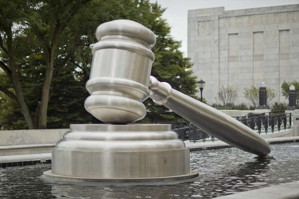 silver gavel sculpture in front of tall building beside grove of trees