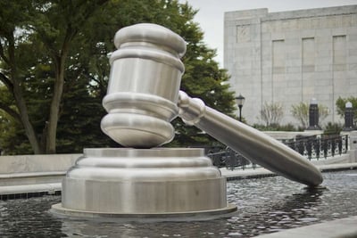 silver gavel sculpture in front of tall building beside grove of trees
